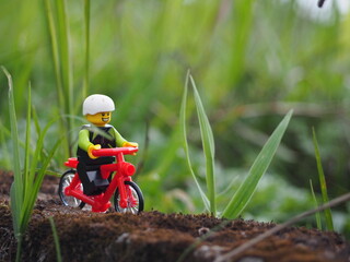 Fototapeta premium Indonesia - November 27, 2019 : Mini toy of action figure at grassland with blurred background. Toy photography concept. Bicycle at outdoor with green grass conceptual design.