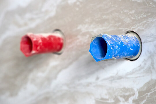 Plumbing pipes with red and blue protection cuffs installed in wall during bathroom renovation, representing hot and cold water line connection interfaces on modern building site.
