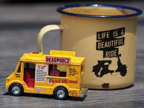 Indonesia - December 9, 2018 : Mini toy of action figure at outdoor with blurred background. Toy photography concept design. Minifigure of Deadpool character from Marvel film with food truck and cup.