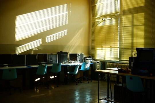 Empty computer lab classroom bathed in golden sunlight filtering through venetian blinds