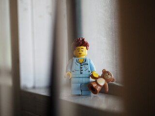 Fototapeta premium Indonesia - September 12, 2025 : Mini toy of action figure at table with blurred background. Miniature photography concept design. Minifigure of people character wearing pajama with teddy bear at home