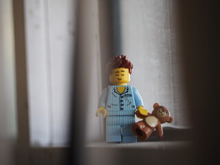 Fototapeta premium Indonesia - September 12, 2025 : Mini toy of action figure at table with blurred background. Miniature photography concept design. Minifigure of people character wearing pajama with teddy bear at home