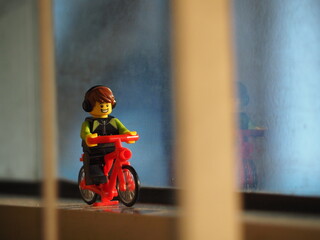 Fototapeta premium Indonesia - September 19, 2019 : Mini toy of action figure at outdoor with blurred background. Miniature photography concept design. Minifigure of young man character riding bicycle at road.