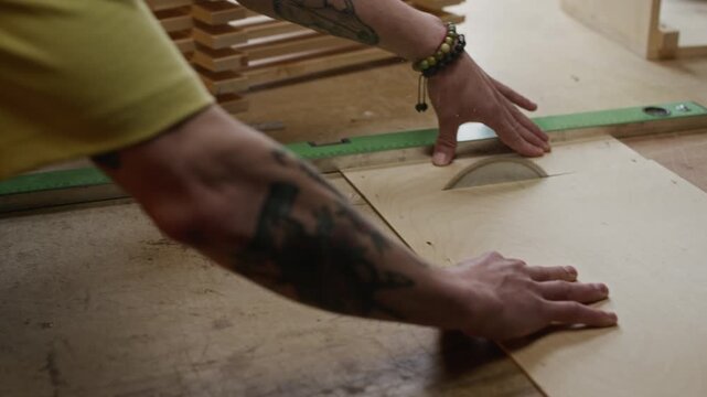 Caucasian young adult male carpenter cutting plywood sheet on circular table saw in workshop. Clip is perfect for woodworking business promotions and trade school advertisements