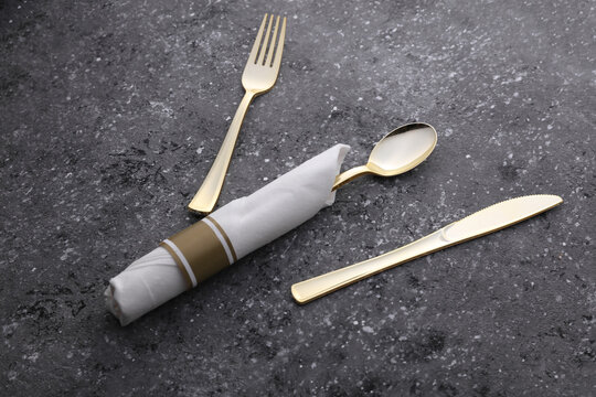 Golden fork, spoon and knife with a rolled napkin on a concrete background. Serving cutlery