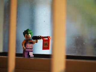 Fototapeta premium Indonesia - September 12, 2025 : Mini toy of action figure at table with blurred background. Miniature photography concept design. Minifigure of Joker clown character with bicycle at sunset time.