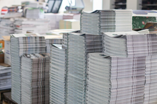 Large stacks of printed newspapers and magazines in commercial printing house. Mass production process in printing industry,  news dissemination, business efficiency.