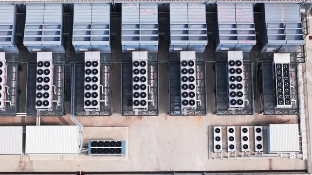 Top-down aerial view of a large data center with rows of industrial cooling systems and air conditioning units working on the rooftop