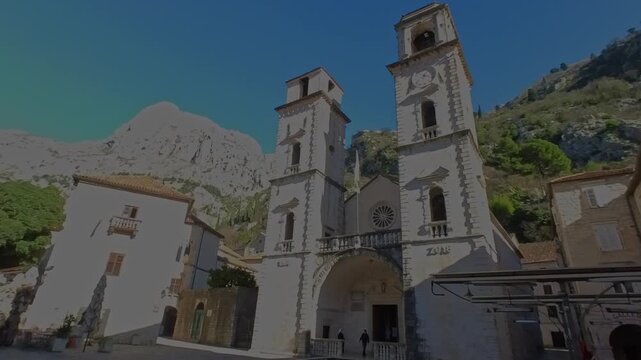 Low angle shot of the historic Saint Tryphon Cathedral facade and bell towers with mountain background in Kotor Old Town, Montenegro.