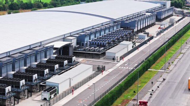 High angle view of a large, modern technology data center with its cooling system. Trucks are loading and unloading goods in the warehouse