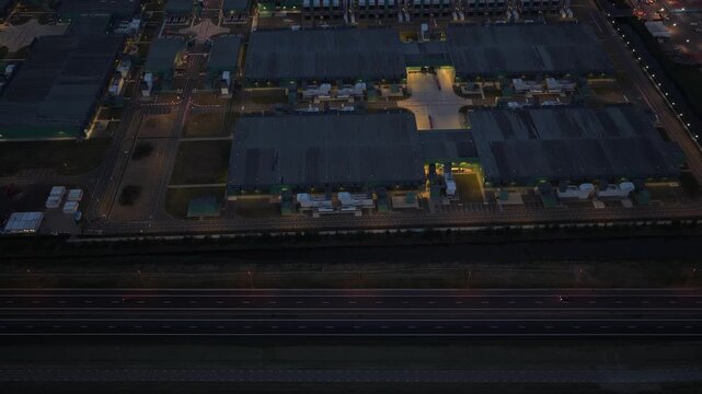 Aerial view of a large, illuminated hyperscale data center complex next to a busy highway. Modern architecture housing cloud computing