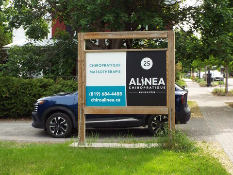 Gatineau, Quebec, Canada &ndash; June 9, 2026: A wooden post sign for "Alinea Chiropratique" advertising "Chiropratique" and "Massoth&eacute;rapie" stands outside along Rue Principale.
