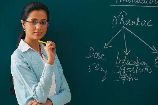 Portrait of confident young teacher against green board 