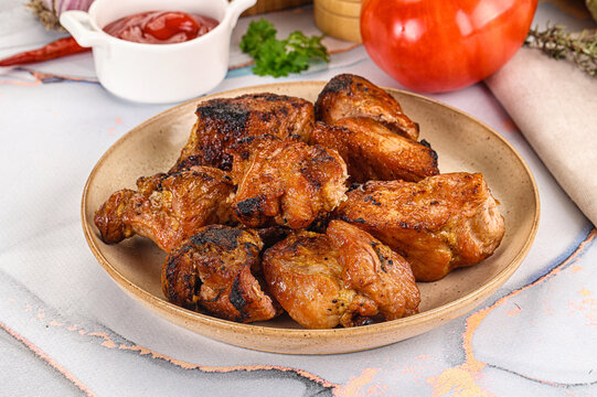 Grilled chicken pieces on ceramic plate with tomato and sauce