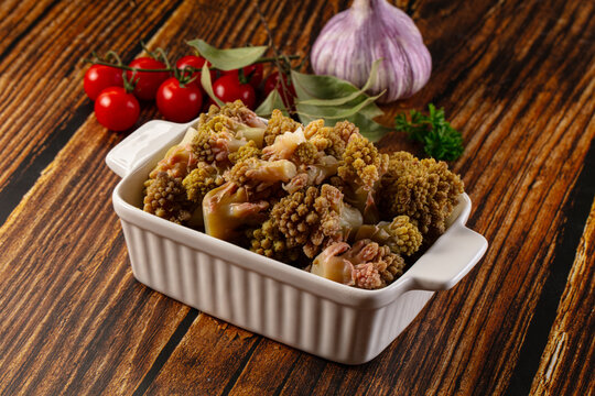 Roasted Roman cauliflower in white ceramic dish with cherry tomatoes and garlic on rustic wood