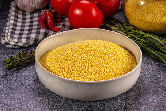 Bowl of uncooked couscous with fresh tomatoes garlic and herbs on dark surface