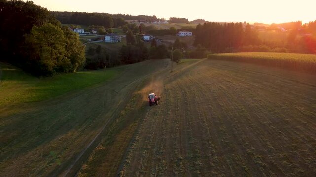 Aerial view of a tractor raking hay in a meadow at golden sunset in a rural landscape