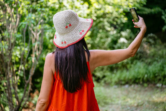 Beautiful woman with straw hat and red dress making selfie with the phone outdoor