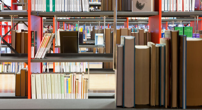 Books on a shelf in a public library, with spaces on the shelves.