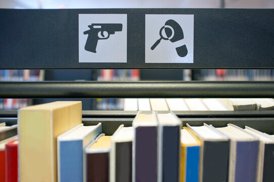 Signs in a public library, the images of a handgun and a magnifying glass over a footprint, symbols for the crime and thriller section.
