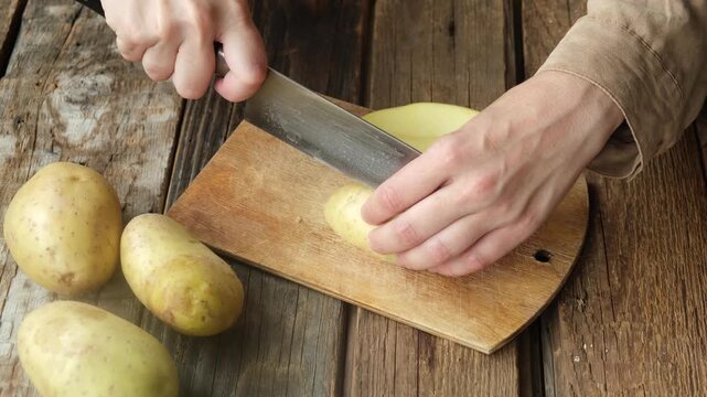 Female hands slicing potato on cutting board. Preparing food.