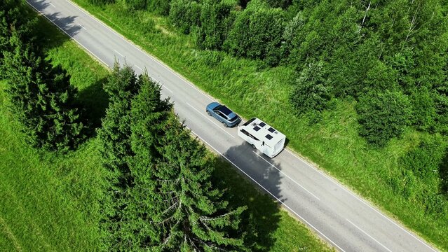Car towing a travel trailer along a tree-lined roadside under bright summer sunlight