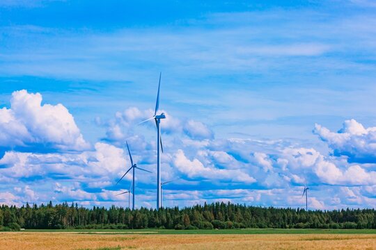 Wind turbines spinning atop green fields under a blue sky filled with clouds in Finland