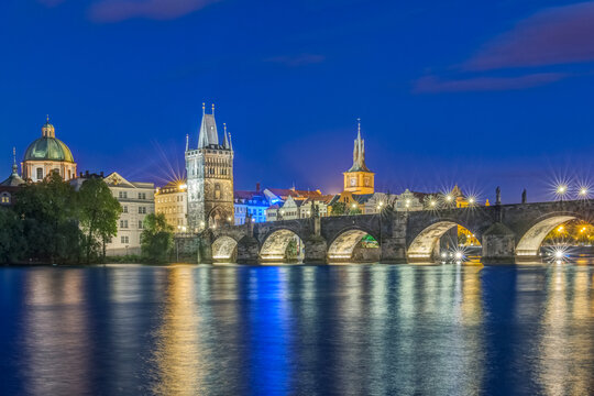 The Charles Bridge over the River Vtlava with buildings lit up at night.