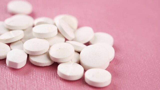 A close up view of numerous white round medicine pills rotating slowly on a vibrant pink background, creating a soothing and rhythmic visual, perfect for health or pharmacy related content