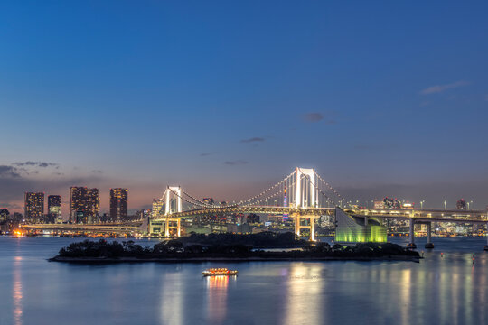 Tokyo, the Odaiba waterfront development at night, reclaimed land with a large bridge and modern buildings and a Statue of Liberty replica.
