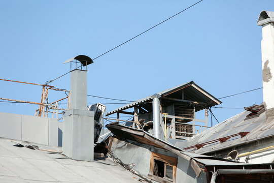  Old city roofs with chimneys, ventilation shafts, tin metal sheets, and wires against a clear blue sky in Nizhny Novgorod. Ideal for roofing repair, renovation, and housing infrastructure.

