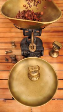 Vertical video social media - Closeup of a man&rsquo;s hand placing an 8 oz weight onto traditional brass mechanical balance scales, with coffee beans pouring into the scoop on the other side.