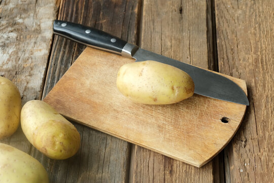 Raw potatoes and a knife on a wooden cutting board