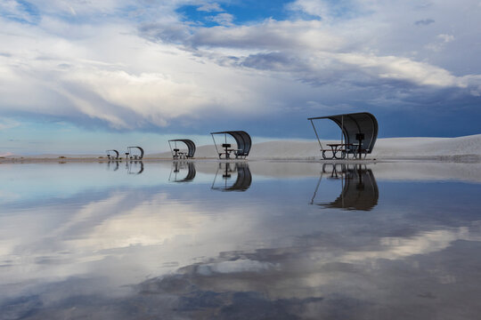 Rows of curved sun shelters, cabanas with seats for visitors at the White Sands national park, reflected in the shallow surface water.