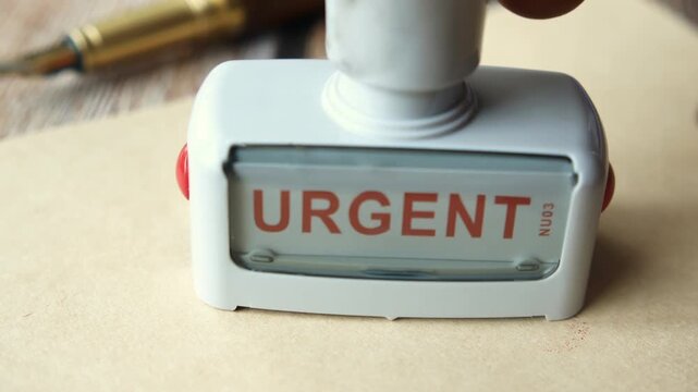 A close-up view of a hand pressing urgent rubber stamp on paper creating a red ink impression to highlight important documents