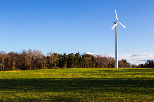 A wind turbine in a rural landscape, fields and trees.