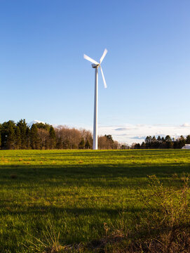 A wind turbine in a rural landscape, fields and trees.