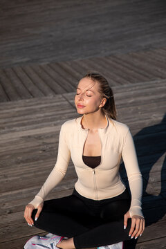 Beautiful woman meditating peacefully with closed eyes outdoors. Young woman sitting cross legged in warm sunlight. Mindfulness wellness concept.
