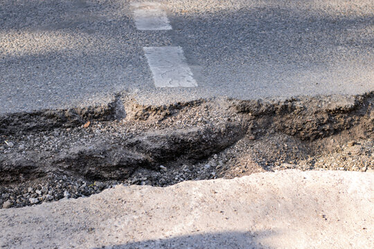 Cracked asphalt road with damaged pavement and lane markings. Ageing infrastructure illustrates concepts of maintenance, transportation, and road safety.