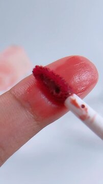 Applying rosy red color on fingertip using a brush. Extreme vertical close up with soft blurred white background. Beauty makeup application concept.