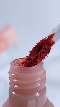 Process of showing a mini red brush being pulled out from pink cosmetic bottle. Front vertical capture for beauty product concept and makeup tool presentation.