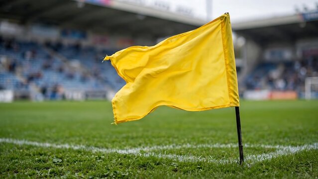 Yellow corner flag waving in the wind on a green grass soccer field with blurred stadium background