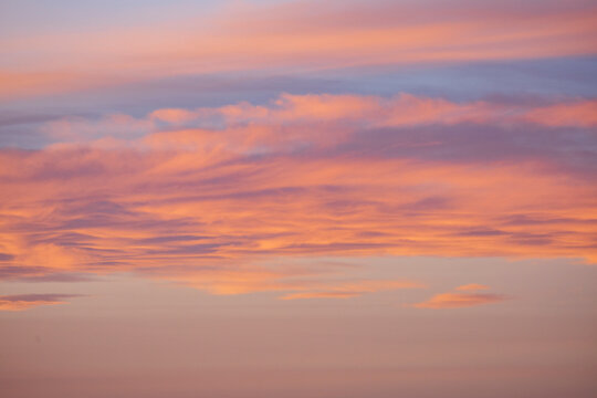 The sky at sunrise above the Chaggaga Sand Dunes, light clouds reflecting red and orange light against blue sky.