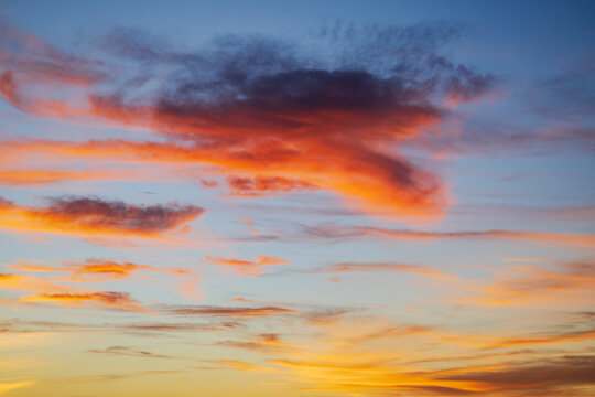 The sky at sunrise above the Chaggaga Sand Dunes, light clouds reflecting red and orange light against blue sky.