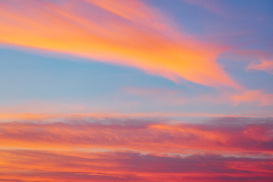 The sky at sunrise above the Chaggaga Sand Dunes, light clouds reflecting red and orange light against blue sky.