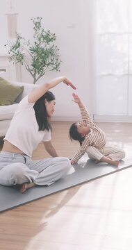 Asian mother and cute daughter doing stretch yoga pose together on a mat at home.