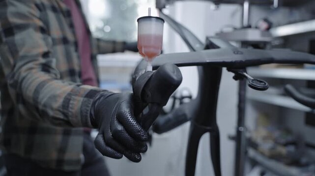 Professional bicycle mechanic bleeding hydraulic disc brakes on a premium black carbon road bike in a workshop. Close-up of bike maintenance, cycling technology and repair service.
