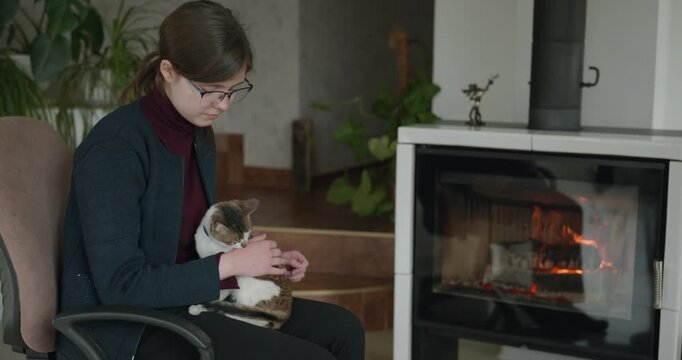 Girl Hold Kitten Tabby Cat on Laps Relaxing Near Fireplace at Home. 4K 10-bit