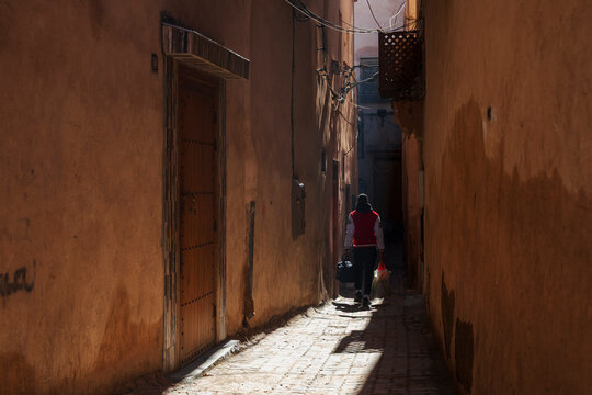 Rear view, a person walking down a narrow alleyway between buildings.