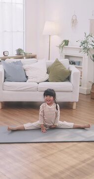 Happy Asian cute little girl doing leg splits exercise on a yoga mat in the living room.